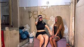A couple shares an intimate outdoor moment in the favela square while a stranger watches from the nearby alley.